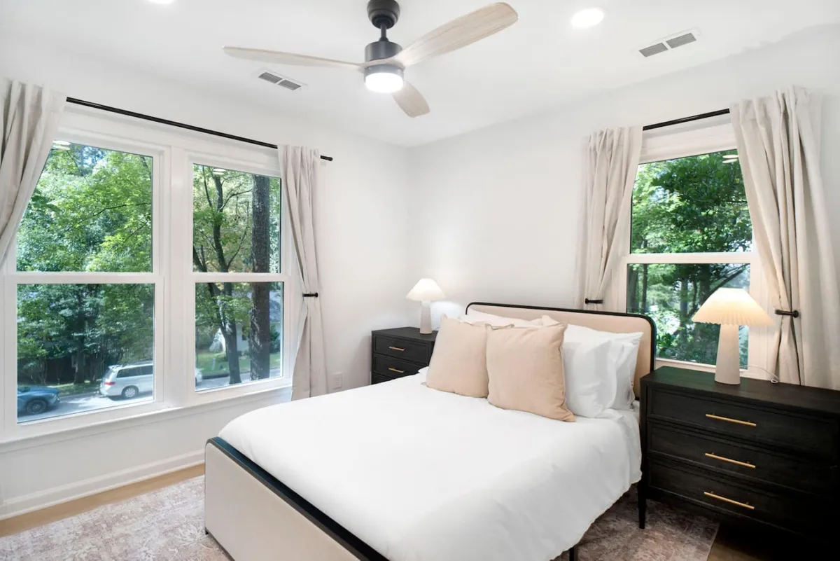 A peaceful bedroom scene featuring a comfortable bed, soft linens, a nightstand with a lamp, and windows that flood the space with gentle daylight. The minimalist decor emphasizes relaxation and privacy.
