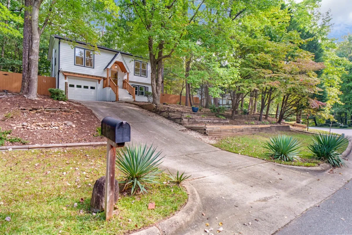 A wide exterior view of the house, driveway, and surrounding greenery, with the mailbox in the foreground. The photo conveys the peaceful neighborhood environment and hints at the ease of access to the city, local eateries, and the greenway for daily walks or commutes.