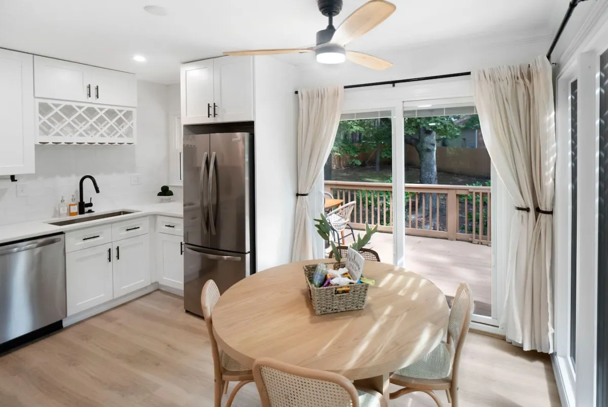 This image showcases the dining table, modern kitchen appliances, and a sliding glass door leading outside. Natural light fills the space, highlighting the open-concept layout and inviting atmosphere ideal for family meals or gatherings.