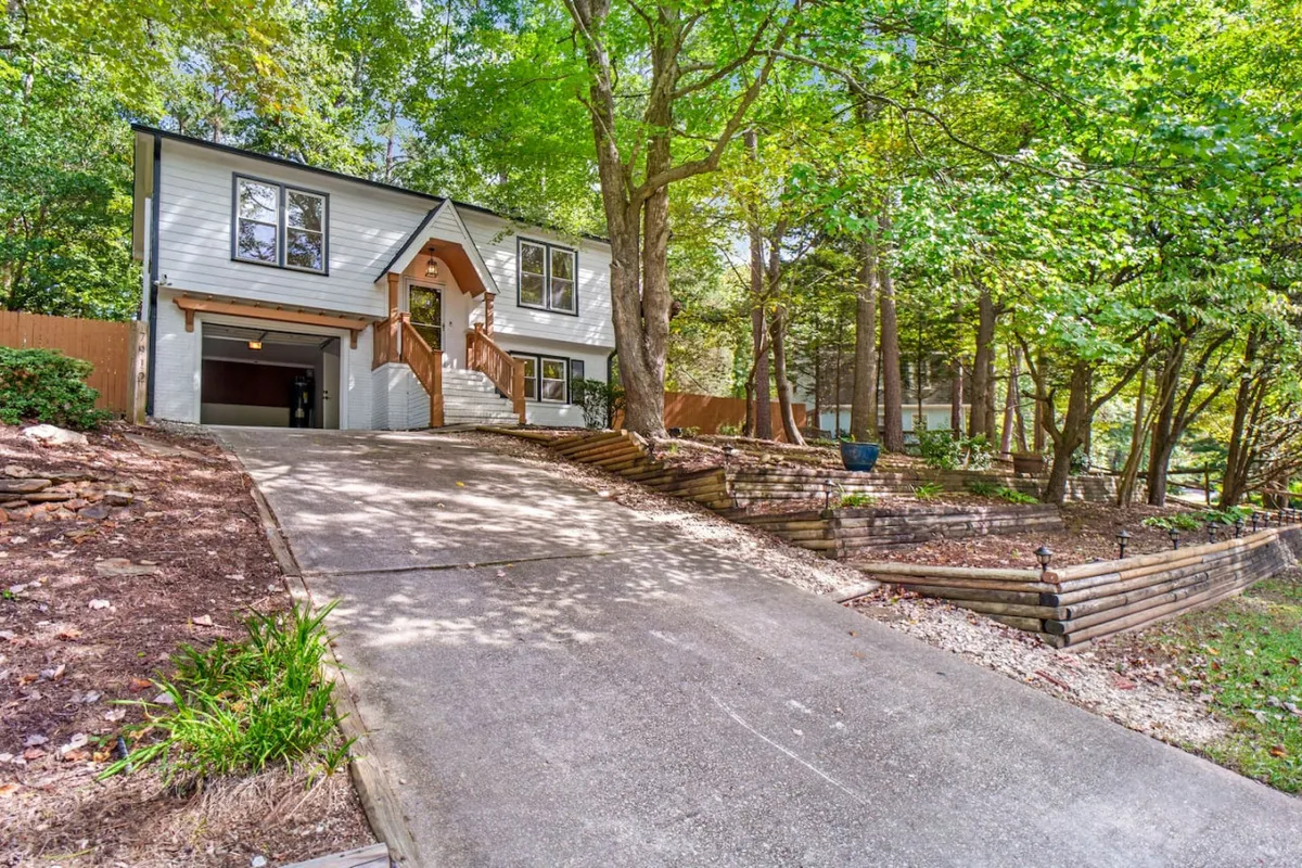 A wide-angle view of the home’s entrance stairs, large windows, and driveway, framed by mature trees. The setting feels serene and inviting, hinting at the nearby parks and natural attractions mentioned in the section.