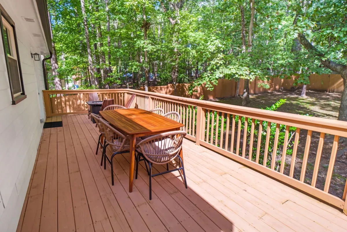 A welcoming wooden deck set with a dining table and chairs, surrounded by lush greenery. The space is ideal for outdoor dining, family gatherings, and relaxing in nature, suggesting a seamless transition between the home and the outdoors.