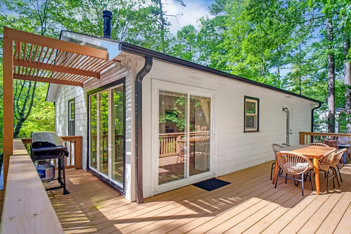 This photo shows a deck area with an outdoor dining table, grill, and large windows, suggesting both relaxation and social dining. The space is styled for comfort, with scenery that hints at gatherings and sunset dinners.