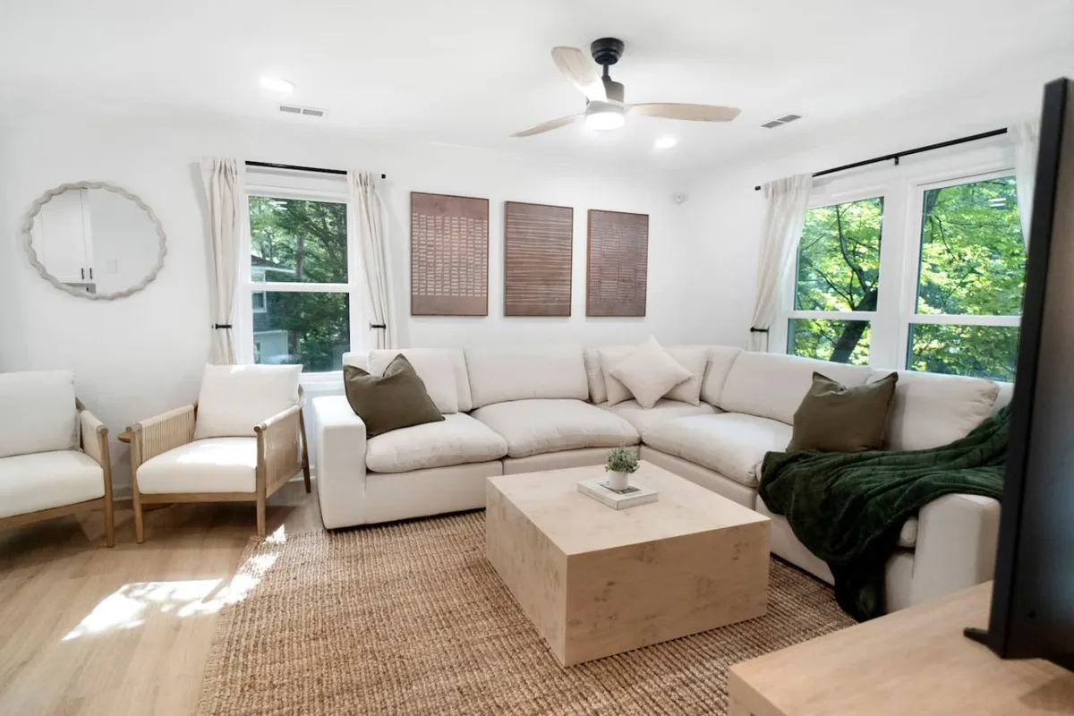 A spacious, comfortable living area with a large sofa, armchairs, coffee table, and ample natural light pouring through the windows. The setup encourages relaxation, conversation, and social activities among groups.