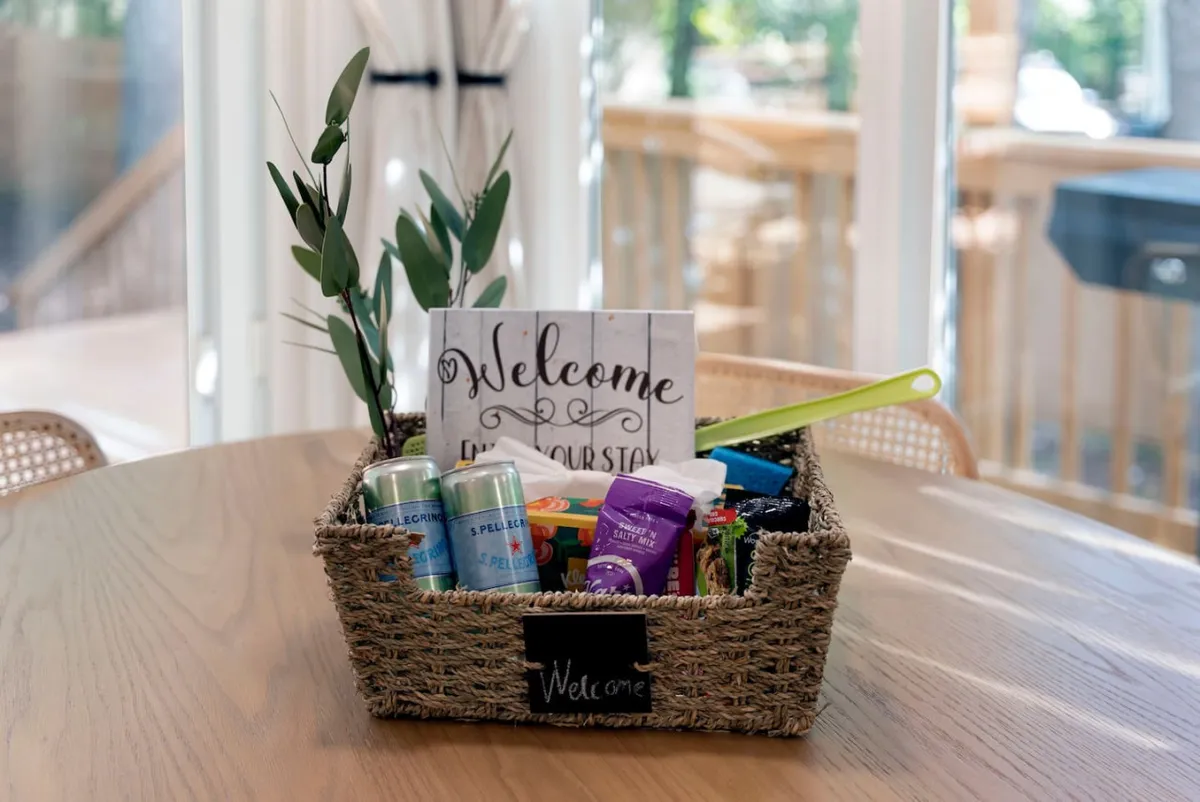 A welcoming scene featuring a beautifully arranged welcome basket and a greeting sign on a table, accented with greenery and a thoughtful table setting. The image radiates hospitality and warmth, inviting guests to gather and connect immediately upon arrival.