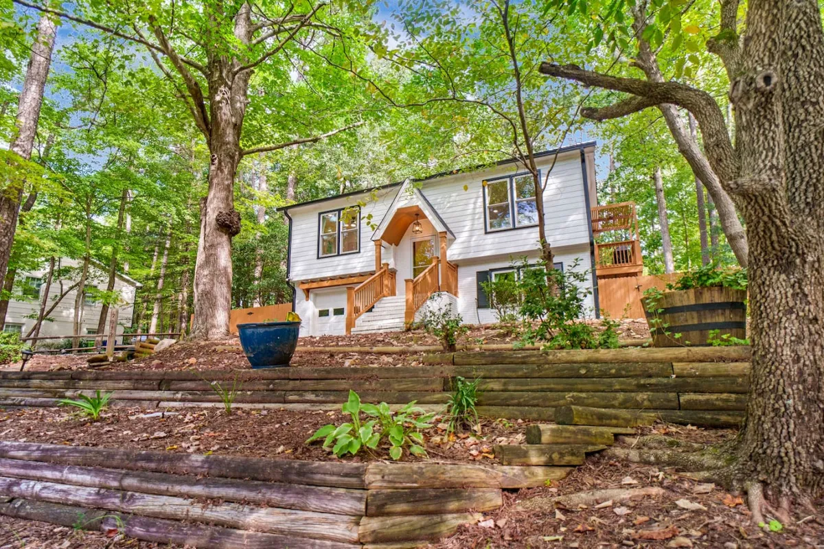 This exterior image features the welcoming front entrance of Brandyapple Retreat, complete with wooden steps, large windows, and a vibrant blue planter. The porch offers a glimpse into the connection between indoor and outdoor spaces, ideal for relaxing while keeping an eye on pets enjoying the yard.