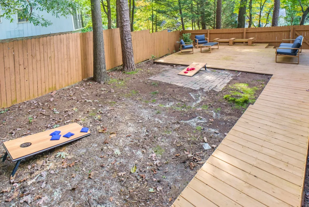 The image features an outdoor seating area set amidst trees, with visible cornhole boards positioned for play. It radiates a playful, inviting atmosphere, perfect for both relaxation and friendly competition.